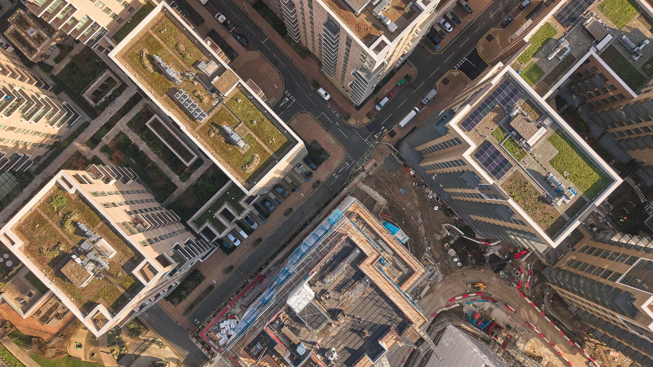 Top-down aerial of a city street junction, green roofs and a live construction plot