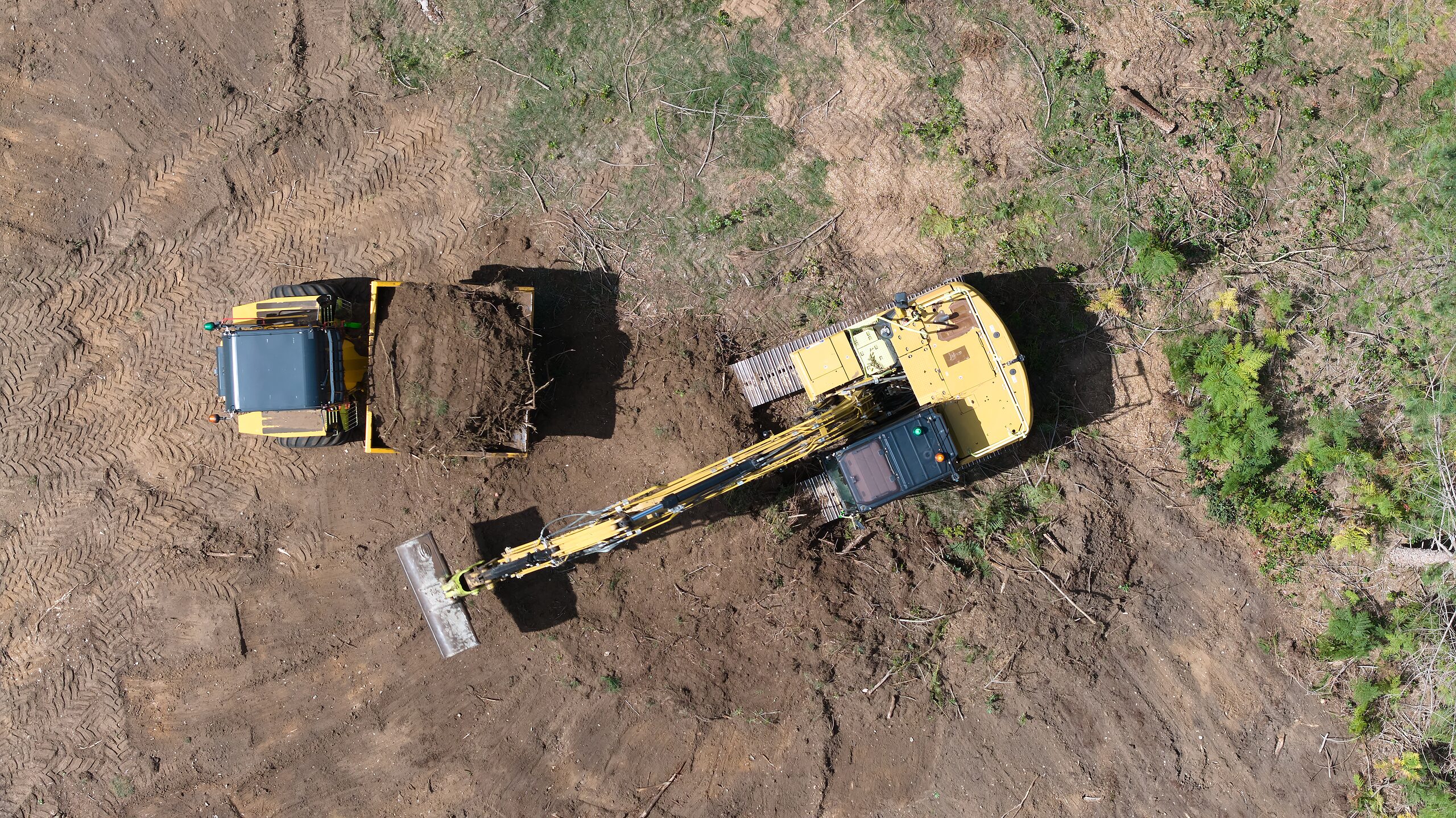 Top-down aerial of an excavator and dumper clearing ground on a development site