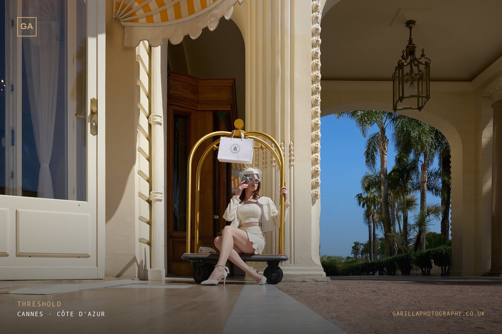 Model on a gold luggage cart at the hotel entrance — titled Threshold