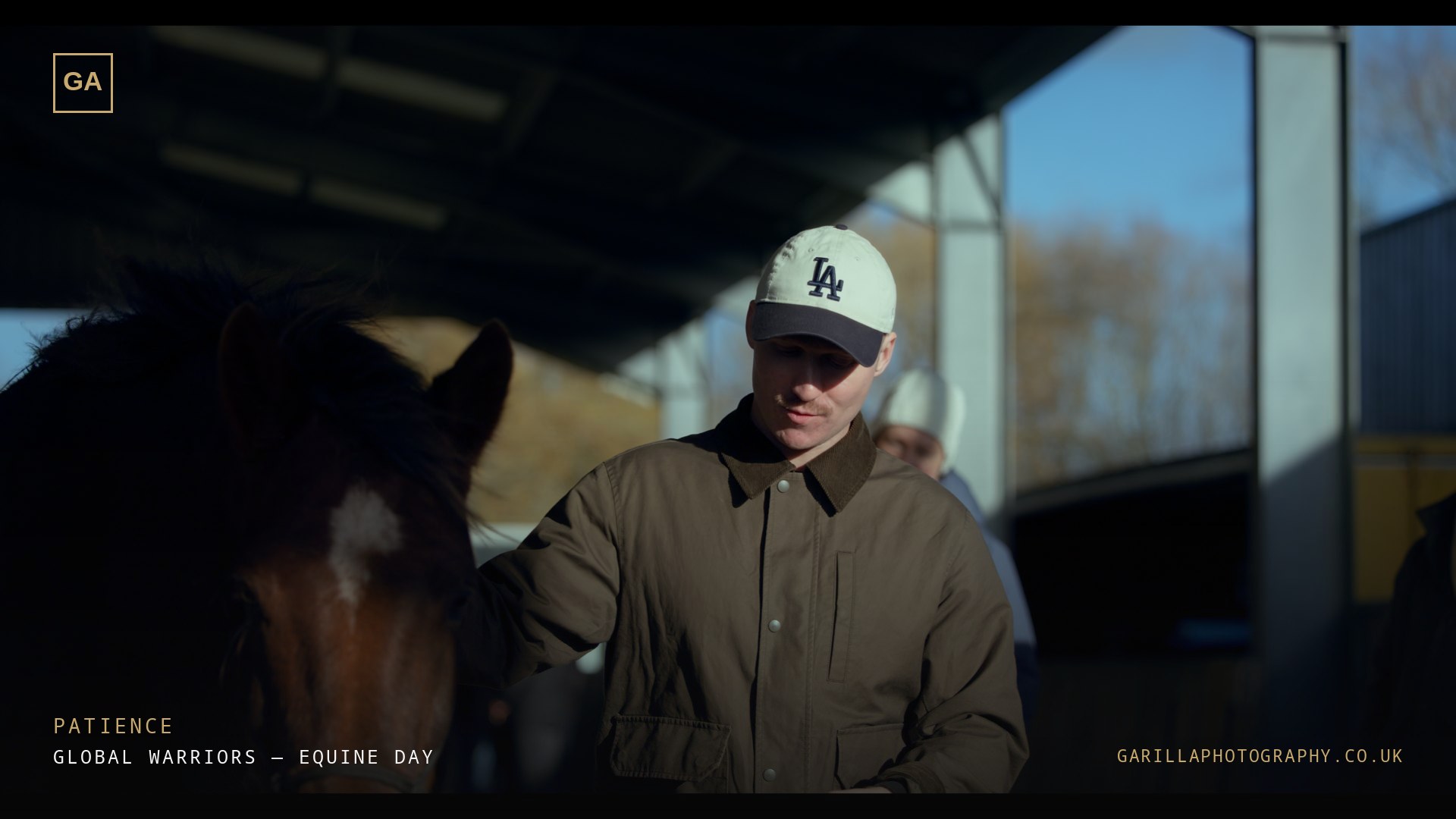 A man in a cap stood calmly with a horse — a still from the film, titled Patience