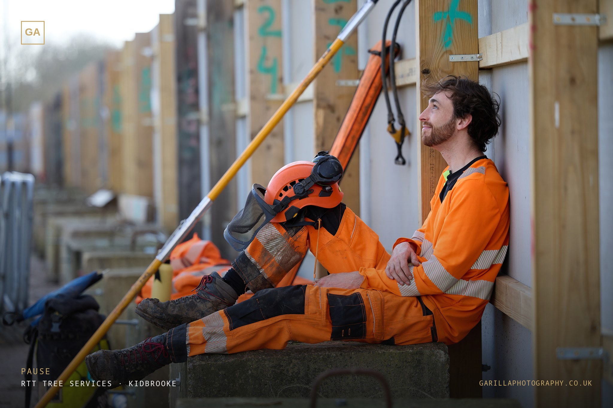 A groundworker resting against site hoarding, helmet off, looking up — titled Pause