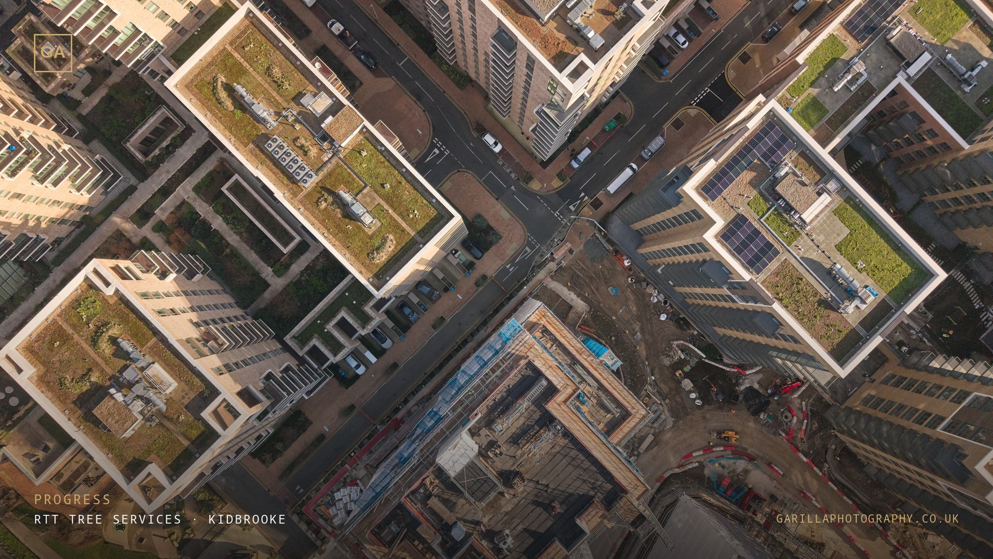 Top-down drone view of the development's rooftops and streets around the site — titled Progress